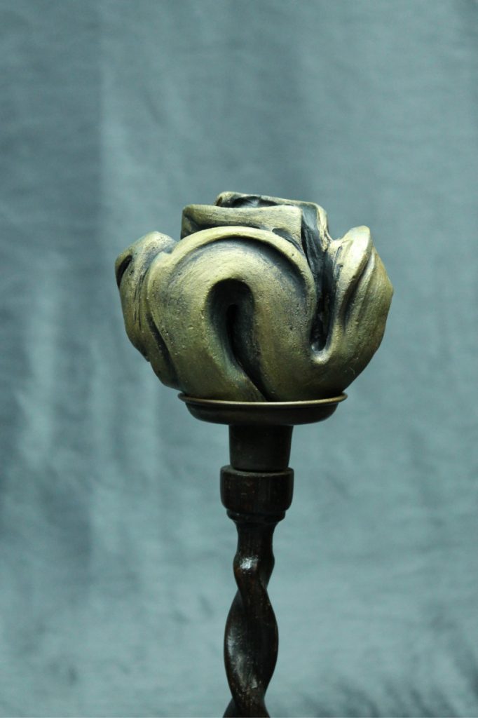 Clay carving of a surreal flower sitting atop a braided wood stem