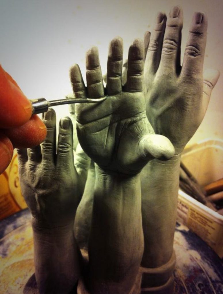 Finely detailed hand carved clay hands and arms reaching up